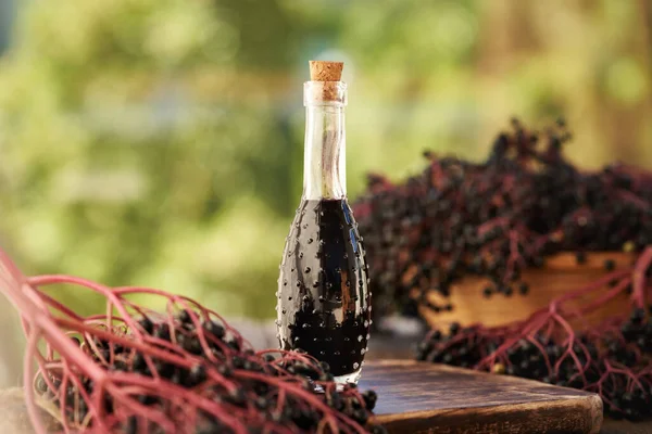 Bir şişe siyah yaşlı şurubu ve açık bir masada taze elderberry.