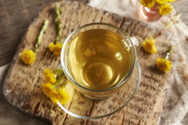 Cam bir fincanda bitki çayı ve bahar başında toplanan taze koza çiçekleri.