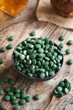 Ahşap bir masanın üzerindeki bir kasedeki alg tabletleri. Sağlıklı besin desteği.