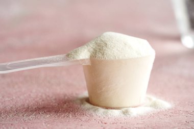 Pembe arka planda plastik bir kaşık içindeki kolajen tozu