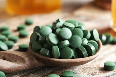 Tahta bir kaşıkta yeşil spirulina alg tabletleri.