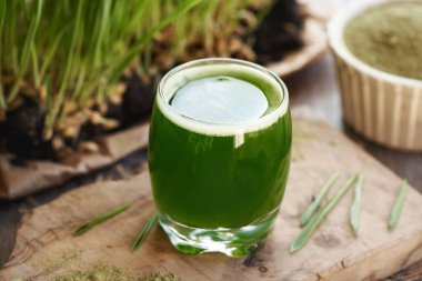 Cam bardakta taze yeşil arpa suyu ve arka planda kendi yetişmiş bıçaklar.