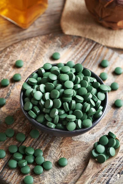 Ahşap bir masanın üzerindeki bir kasedeki alg tabletleri. Sağlıklı besin desteği.