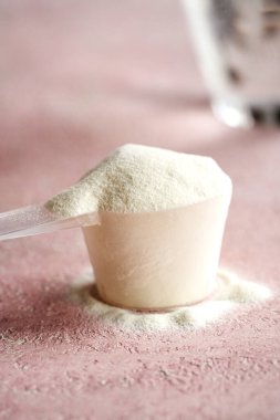 Plastik bir kaşık içindeki kolajen tozu ve arka planda bir bardak su.