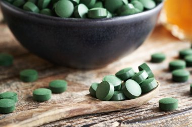 Tahta bir kaşıkta ve masada bir kasede, alg tabletleri.