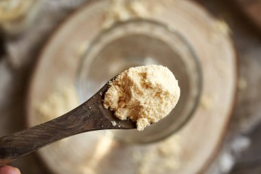 Beyaz protein tozu bir bardak suyun üzerindeki tahta kaşıkta.