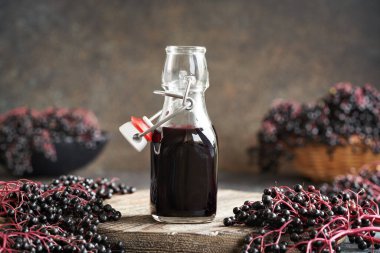 Bir şişe siyah yaşlı şurubu ve masada taze elderberry.