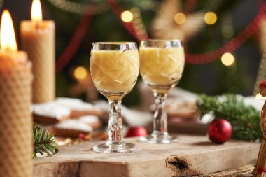 İçinde mumlar, Noel ağacı ve masa süsleri olan iki kesik cam bardakta Eierkonyak.