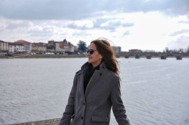Gri ceketli kadın tarihi Macon Fransa ve Saone Nehri manzaralı nehir kıyısında yürüyor.