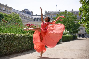 Güneş ışığı altında akan mercan elbiseyle dans eden balerin.