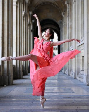 Kırmızı elbiseli balerin Louvre kemerlerinin altında büyük jete gösterisi yapıyor.