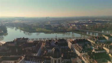 İnsansız hava aracı görüntüleri barok kilise ve geleneksel kiremitli çatıları gösteriyor. Su yolu ve kentsel alan yumuşak sabah ışıltısı altında. 