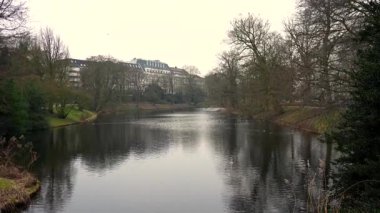 Sakin park gölünün huzurlu kış manzarası çıplak ağaçlar ve şehir binalarıyla çevrili Bremen Almanya 'sında sakin mevsimlik manzara altında yumuşak gün ışığında durgun suya yansıyor.