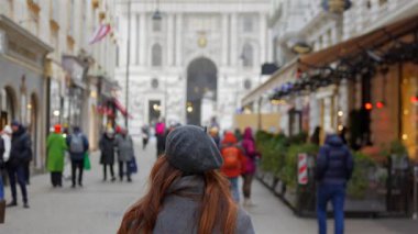 Uzun kızıl saçlı bir kadının kışın Avusturya Viyana 'da lüks bir alışveriş caddesinde yürümesi.