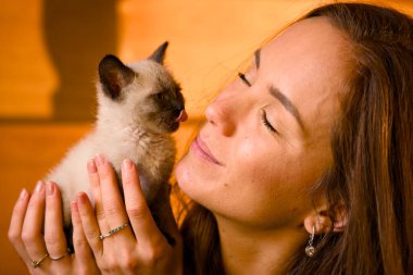 Gülümseyen kadın, küçük siyam kedisine nazikçe sokuluyor.
