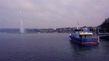 17 Şubat 2025 'te Cenevre Gölü' nden geçen yolcu gemisi bulutlu gökyüzünün altında Jet d Eau ve sahil boyunca uzanan şehir binalarıyla birlikte.