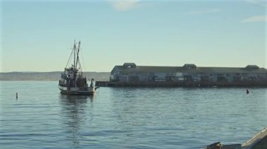 Monterey California 'daki bir rıhtıma sakin deniz ışığı ve sanayi kıyısı binalarıyla gelen balıkçı teknesi.