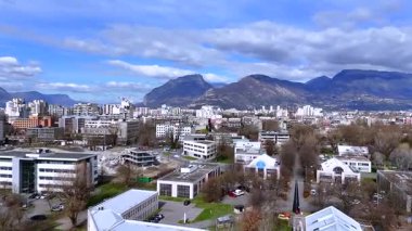 Grenoble 'un düşük drone görüntüsü, göbek blokları, ağaç sıralanmış caddeler, yıkım alanı ve dağlar.