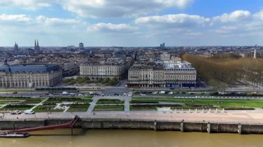 Garonne nehir kıyısında tarihi taş binalar, nehir kenarındaki bahçeler, işlek yollar ve parçalı bulutlu bir gökyüzünün altındaki çamurlu nehir.
