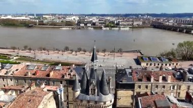 Bordeaux Porte Cailhau 'nun insansız hava aracı videosu ortaçağ kapısı, dar eski cadde, taş binalar ve güneşli bir bahar gününde nehir kenarındaki gezinti alanında aktif trafik.