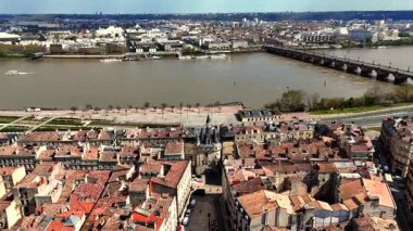 Ortaçağ Porte Cailhau kapısının, tarihi çatıların ve Pont de Pierre taş köprüsünün çamurlu Garonne nehrinin üzerindeki parçalı bulutlu gökyüzünün altındaki insansız hava aracı videosu.