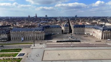 Bordeaux 'nun eski kasabasının insansız hava aracı videosu Porte Cailhau ortaçağ şehir kapısı, taş çatılar, nehir kenarındaki gezinti güvertesi ve parlak parçalı bulutlu bahar gökyüzü altında aktif trafik