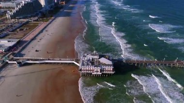 Daytona Sahili 'nin okyanus sörfü kumlu sahil kıyısı ve gündüz vakti deniz kenarında gezinti yapan insansız hava aracı görüntüsü.