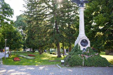 Güneşli bir günde Cakovec şehir parkında bronz kartal heykeli ve yeşil çelenklerle tarihi beyaz taş savaş anıtı