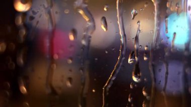Bulanık şehir ışıklarıyla cam üzerine yağmur damlaları ve su