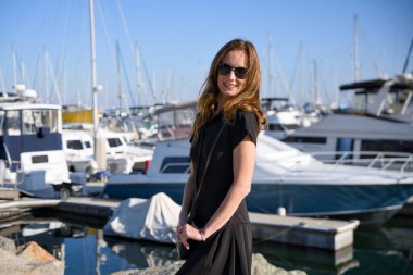 Güneşli bir günde marinada yatların yanında poz veren mutlu kadın.