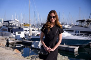 Kaliforniya 'daki güneşli marinada yatların yanında neşeli bir kadın.