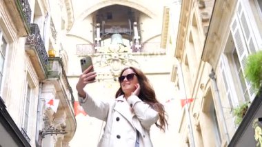 Dar Bordeaux caddesinde tarihi binaların bayraklarıyla selfie çeken kadın.