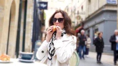 Güneş gözlüklü kadın Bordeaux Caddesi 'ndeki açık kafede kruvasan yiyor.