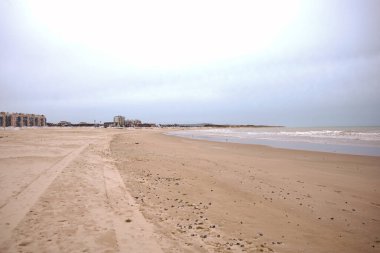 Kıyı şeridi ve uzak binaları olan geniş, boş bir sahil Calais France