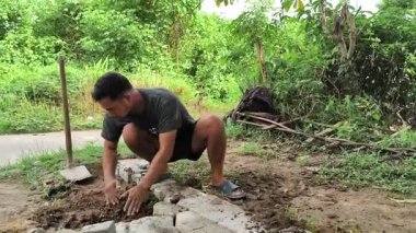 Asyalı bir adam yeri çapalıyor ve beyaz tuğlaları düzleştiriyor.