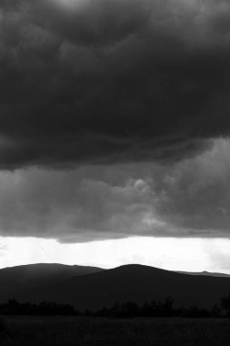 Dramatik fırtına bulutlarının ve yağmurun uzak dağlara düşüşünün siyah beyaz fotoğrafı.
