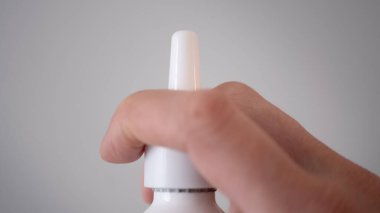 Arka planda beyaz bir burun spreyi tutan bir elin yakın çekimi. Soğuk algınlığı, alerji nöbeti, burun tıkanıklığı ve sağlık ürünleri kavramı. İlaç reklamları, tıbbi bloglar, online eczane görselleri ve iyileştirme için ideal.