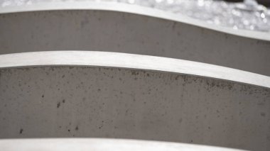 Kavisli beton elementlerin yakın çekimi soyut bir mimari model oluşturuyor. Tekrarlayan çizgileri ve yumuşak gölgeleri olan minimalist modern tasarım. Mimarlık, yapı, biçim, doku ve kentsel minimalizm kavramı.