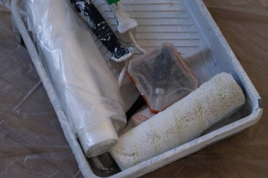 Tablada, yerde koruyucu plastik film olan boya aletleri. Patenler, fırçalar ve kaplama malzemeleri iç yenileme için düzenlenir. DIY, inşaat ve ev geliştirme temaları için kullanışlı.