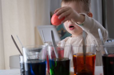 Çocukların evde paskalya yumurtası boyadığını gösteren yürek ısıtan bir dizi. Kırmızı, mavi, yeşil ve turuncu boyalı bardaklar, beyaz ve bıldırcın yumurtaları ve küçük boyalı eller Paskalya hazırlığının yaratıcı ruhunu yansıtıyor. Her an merakı yansıtıyor, duyusal p