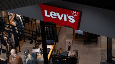 Krakow, Polonya, Ekim 2025. Katlanmış kot pantolonlar, ceketler ve aydınlatma işareti altında günlük kıyafetler içinde mankenlerin yer aldığı bir Levis mağazasının iç manzarası. Modern perakende tasarımı ve küresel moda markasını temsil eden editoryal görüntü. Düzenle