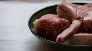 Pişirmek için hazırlanan çiğ domuz pirzolası, beyaz bir mutfak yüzeyindeki yeşil bir kaseye konur. Görüntü, sade, ev yapımı bir yemek pişirme konseptini taşır ve gıda, aşçılık veya tarifle ilgili projelerde kullanılabilir..