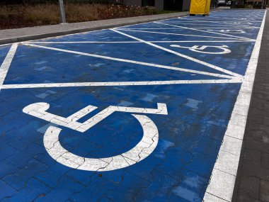 Asfaltlı yüzeyde beyaz erişilebilirlik sembolleriyle işaretlenmiş bir sıra mavi engelli park yeri. Görüntü kentsel altyapı, kapsayıcı tasarım ve hareketlilik erişilebilirlik standartlarını vurguluyor