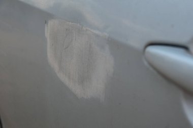 Kapı kolunun yanında görünen bir boya yamasını gösteren bir arabanın yakın görüntüsü. Görüntü araç yüzeyindeki hasarı, bakımı, restorasyon sürecini ya da bitmemiş onarımları gösteriyor. Uygun.