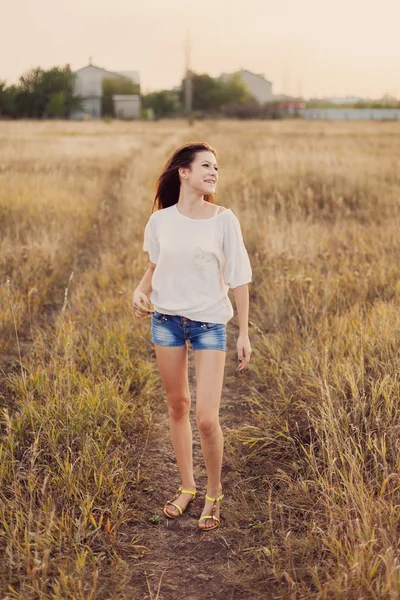 Chica joven con el pelo largo y castaño permanecer en el prado, sonriendo — Foto de Stock