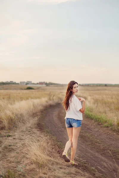 Chica joven con el pelo castaño largo caminando lejos en el camino — Foto de Stock