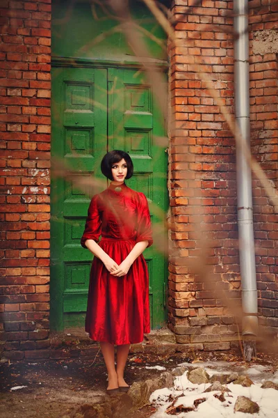 Дівчина брюнетка в червоній вінтажній сукні стоїть біля старих дверей . — стокове фото