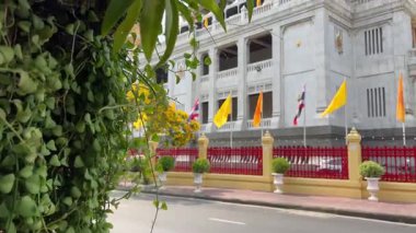 Bangkok 'taki altın tapınağı çevreleyen çitlerin üzerinde çeşitli renkli bayraklar asılı. Parlak sarı turuncu ve beyaz mavi bayraklar rüzgarda dalgalanıyor kutsal pagoda bölgesinde canlı kültürel sahneler yaratıyor.