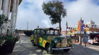 Ba Na Hills Vietnam eğlence parkında siyah ve kırmızı çatıları olan kalenin yakınına park edilmiş ayçiçekleri ile süslenmiş renkli yeşil bir araba. Manzaralı Da Nang Vietnam 10.27.2025 manzaralı neşeli bir sahne.