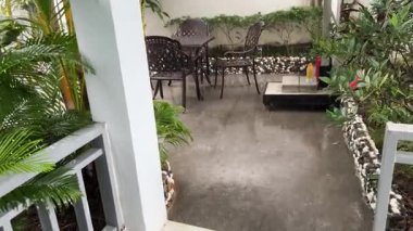 Yağmurlu bir günde bahçe mobilyaları. Boş masa ve sandalyeler nemli, sisli bir orman zeminine kurulmuş, yemyeşil ve bulutlu gökyüzü ile sakin bir atmosfer yaratıyor. Yüksek kalite 4k